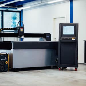 En stor Hugong 1,5 x 3 m Intecut-HT styrd plasma med vattenbord och dess kontrollenhet placeras i en rymlig, väl upplyst verkstad med blå överliggande strukturer och ett fönster.